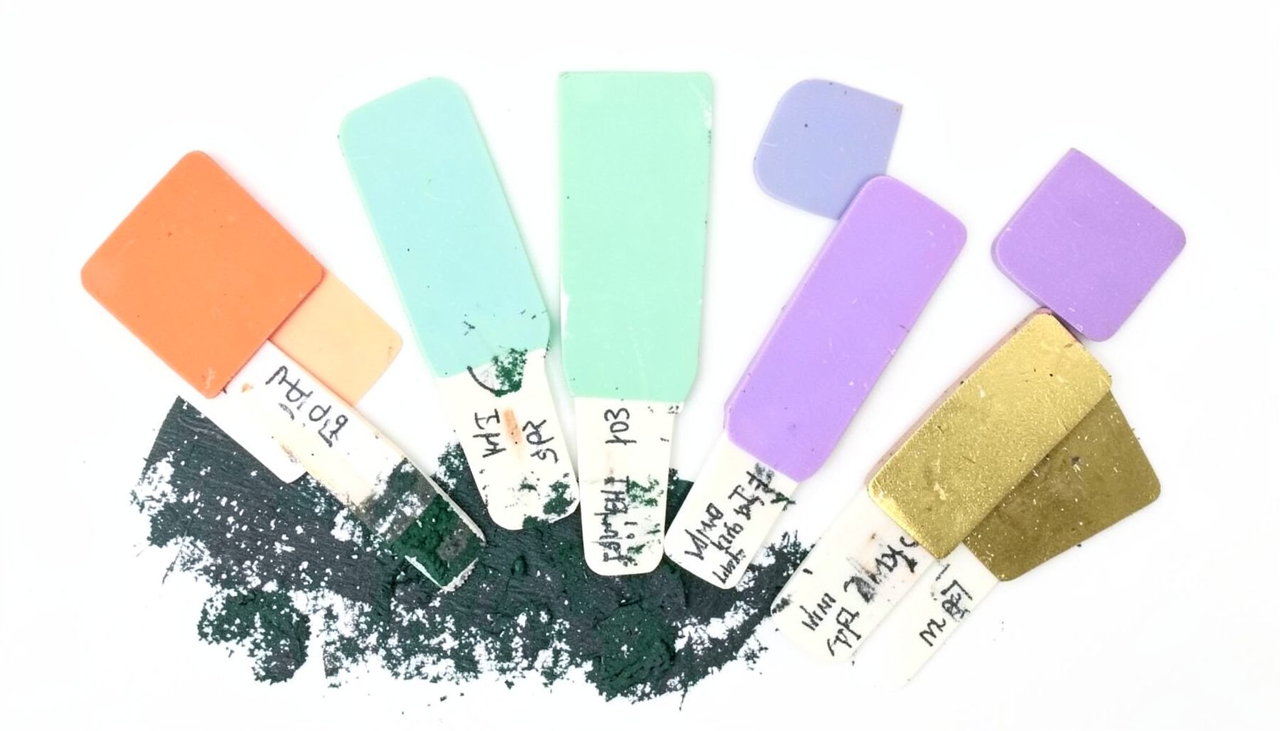 A collage of colourful square nail swatch sticks fanned out across a white background, each painted in a different shade — coral, mint, lavender, and gold — with handwritten labels beneath.