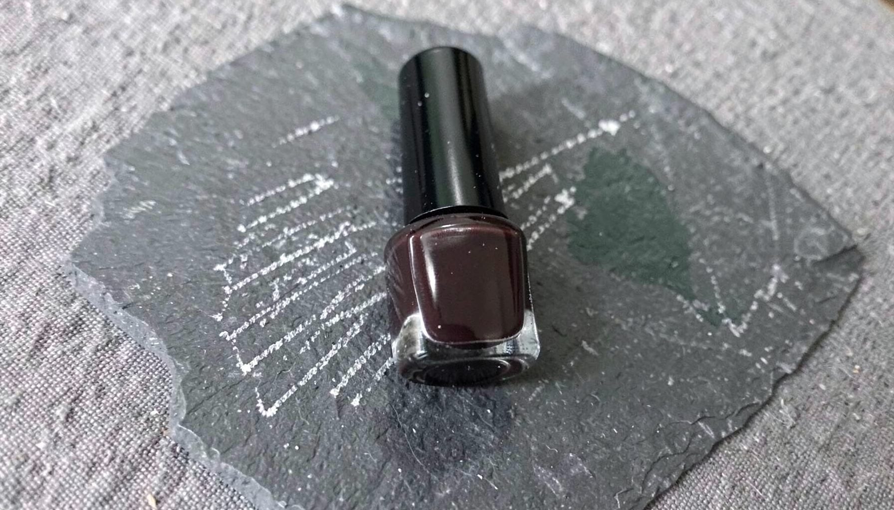 A single bottle of deep charcoal nail polish with a glossy cap, resting on a textured grey fabric background.