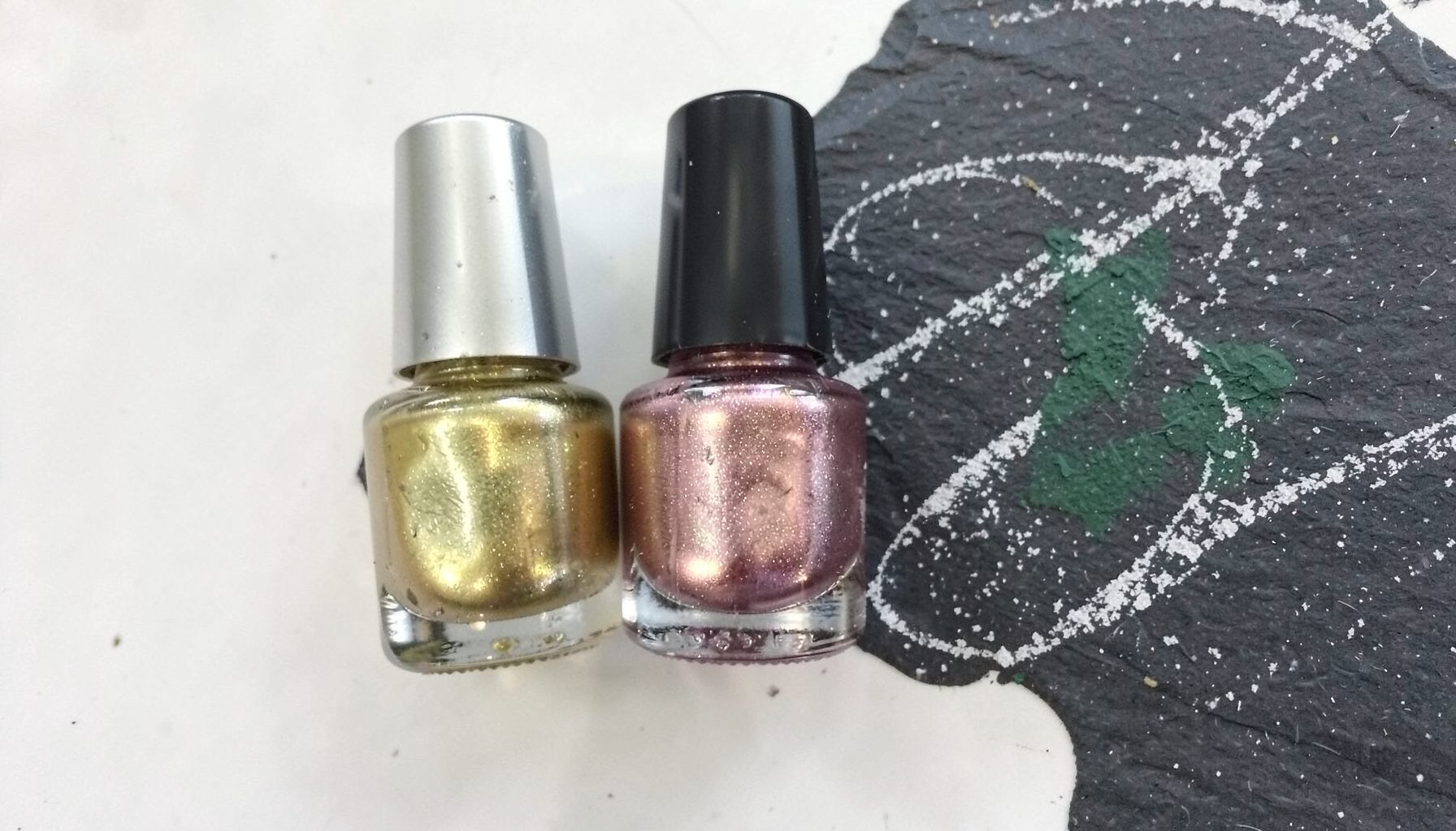 Three bottles of metallic nail polish in gold, silver, and rose-gold tones lined up on a white surface, reflecting soft light.