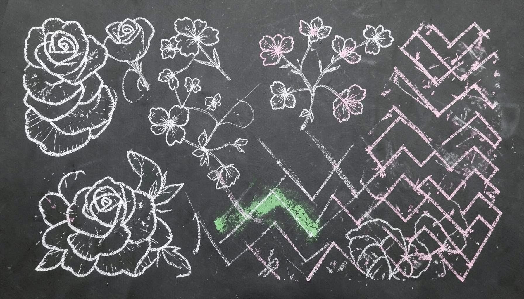 A dark slate chalkboard covered in hand-drawn nail-art sketches: swirling roses, cherry blossoms, and geometric chevron patterns in white and pale pink chalk, with a few smudged eraser marks adding texture.